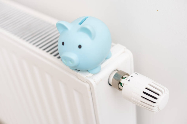 Piggy bank on heating radiator against light background. Space for text - Photo, Image