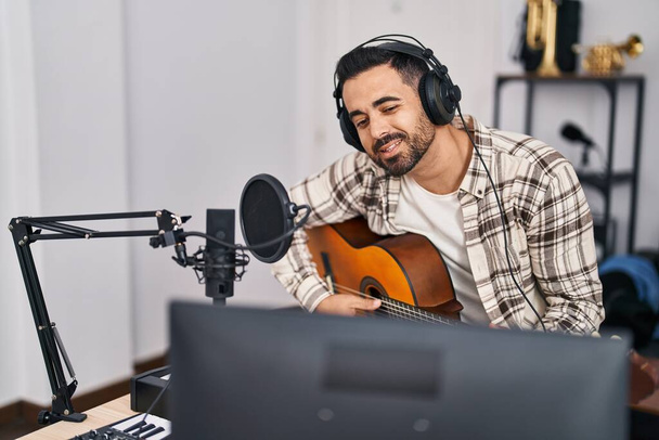 Joven artista hispano cantando una canción tocando la guitarra en un estudio de música - Foto, imagen