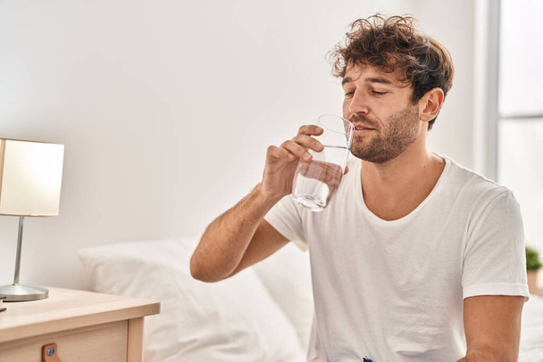 Hombre joven bebiendo agua en el dormitorio - Foto, imagen