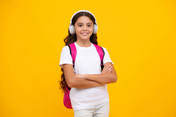 Iskolás lány, tinédzser hallgató fülhallgatóban, sárga, elszigetelt stúdió háttérrel. Iskolai és zenei nevelési koncepció. Vissza az iskolába. - Fotó, kép