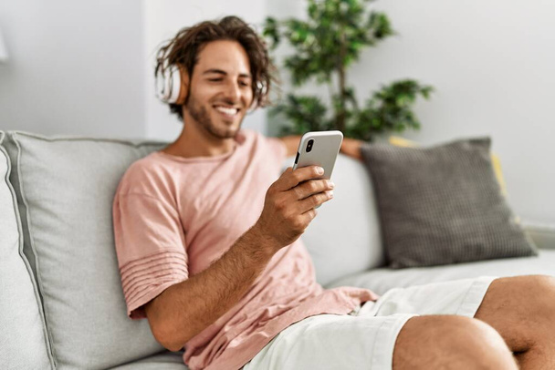 Νεαρός ισπανόφωνος ακούγοντας μουσική χρησιμοποιώντας smartphone στο σπίτι. - Φωτογραφία, εικόνα