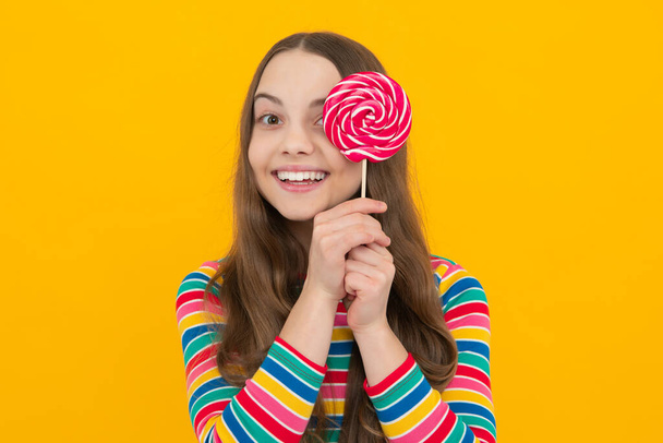 Teenager girl eating sugar lollypop. Candy and sweets for kids. Child eat lollipop popsicle over yellow isolated background. Yummy caramel, candy shop - Photo, Image