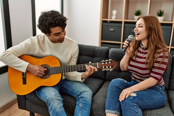 Young couple playing classical guitar and singing using microphone at home. - Foto, afbeelding
