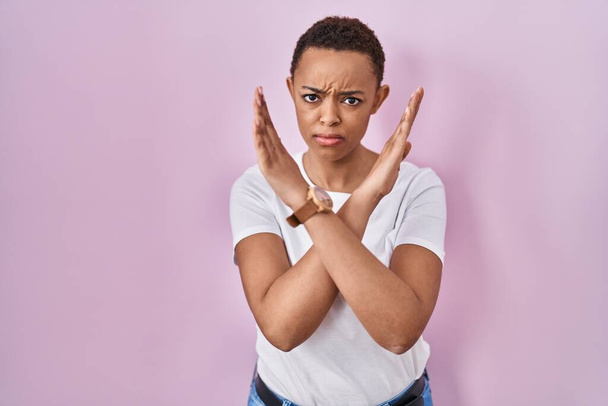 Hermosa mujer afroamericana de pie sobre la expresión de rechazo de fondo rosa cruzando brazos haciendo signo negativo, cara enojada  - Foto, imagen
