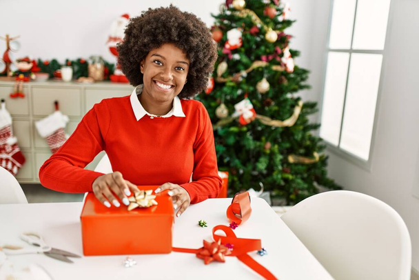 Fiatal afro-amerikai nő mosolygós magabiztos csomagolás karácsonyi ajándék otthon - Fotó, kép