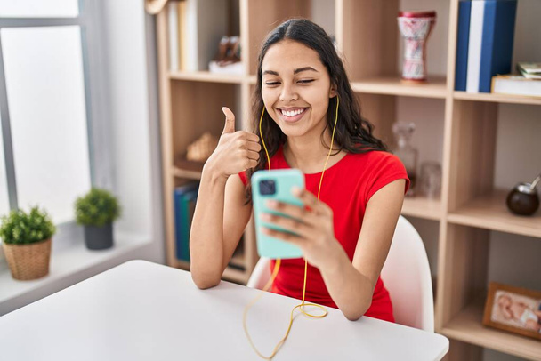 Молода бразіліанка робить відеодзвінок зі смартфоном, усміхаючись щасливим і позитивним, великим пальцем, роблячи відмінний знак схвалення.  - Фото, зображення
