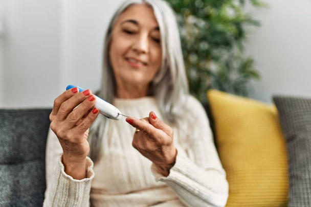 Жінка середнього віку сіроока посміхається впевнено вимірюючи глюкозу в домашніх умовах
 - Фото, зображення