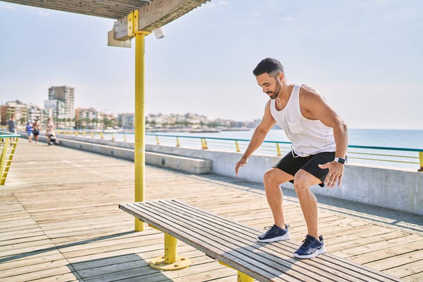 Hombre hispano haciendo ejercicio saltando a un banco al aire libre en un día soleado - Foto, Imagen