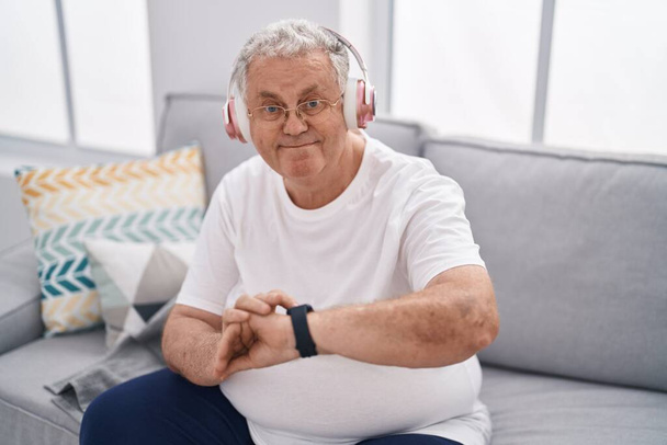 Middelbare leeftijd grijsharige man luisteren naar muziek kijken horloge thuis - Foto, afbeelding