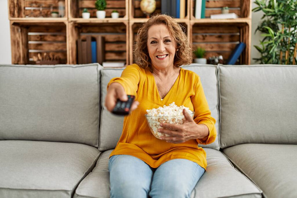 Mulher caucasiana de meia idade assistindo filme sentado no sofá em casa. - Foto, Imagem