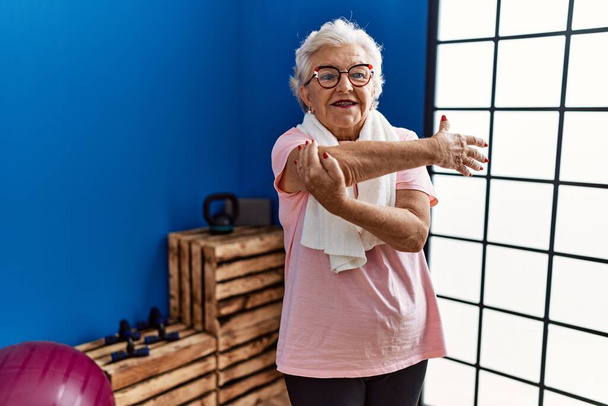 Starsza siwowłosa kobieta ubrana w odzież sportową uśmiechnięta pewnie stojąca w centrum sportowym - Zdjęcie, obraz