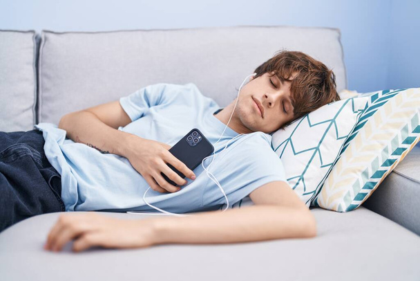 Junger blonder Mann hört Musik und schläft zu Hause auf dem Sofa - Foto, Bild