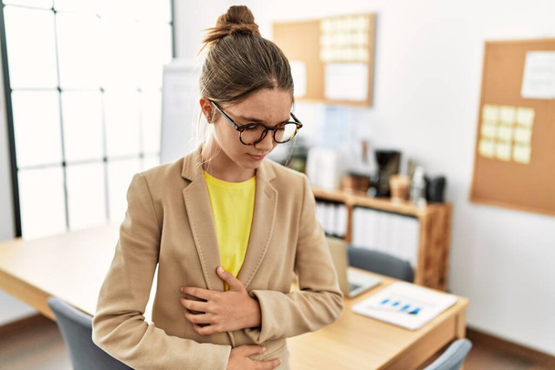 Young brunette teenager wearing business style at office with hand on stomach because nausea, painful disease feeling unwell. ache concept.  - Valokuva, kuva