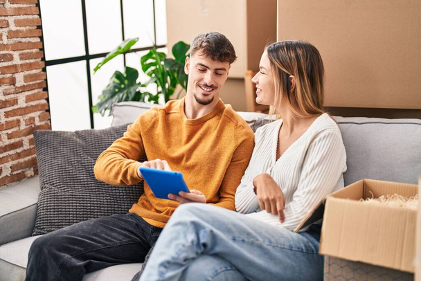 Young man and woman couple using touchpad sitting on sofa at new home - Foto, Bild