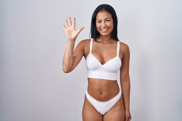 Mujer hispana vistiendo lencería mostrando y señalando con los dedos el número cinco mientras sonríe confiada y feliz.  - Foto, Imagen