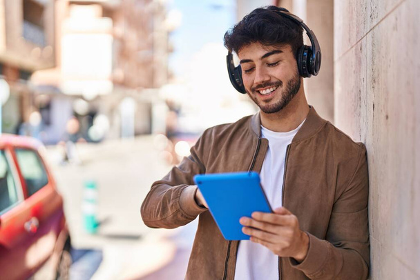 Junger hispanischer Mann lächelt selbstbewusst mit Touchpad auf der Straße - Foto, Bild