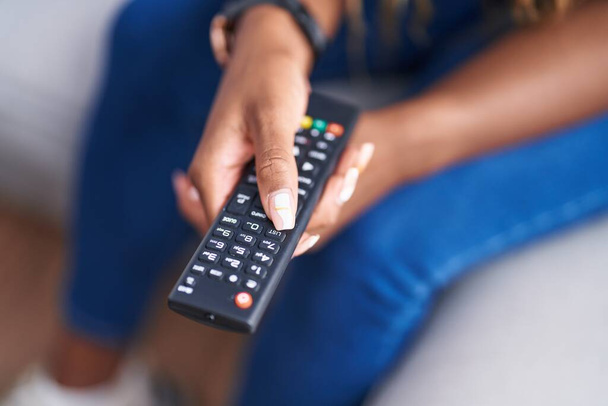 Afro americana mujer sosteniendo tv control remoto sentado en sofá en casa - Foto, imagen