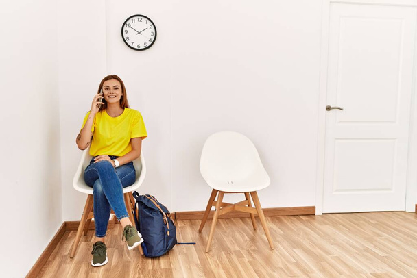 Young woman student talking on the smartphone sitting on chair at waiting room - Photo, Image