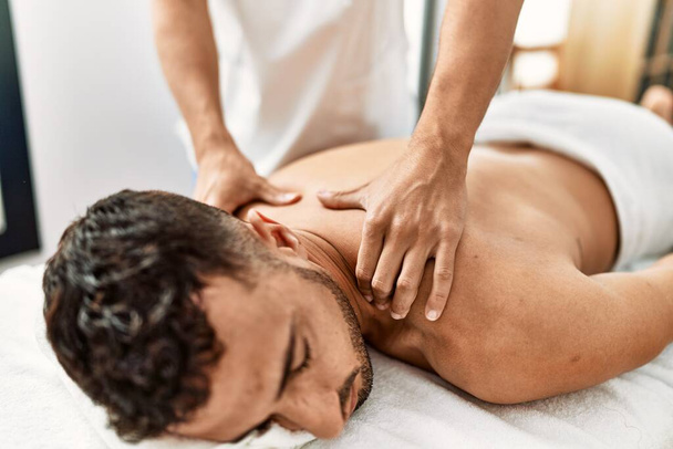 Due uomini ispanici fisioterapista e paziente avendo sessione di riabilitazione massaggiare indietro al centro di bellezza - Foto, immagini