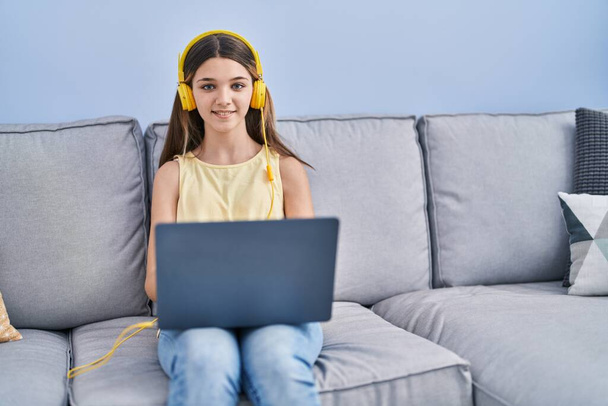 Αξιολάτρευτο κορίτσι που χρησιμοποιεί φορητό υπολογιστή κάθεται στον καναπέ στο σπίτι - Φωτογραφία, εικόνα