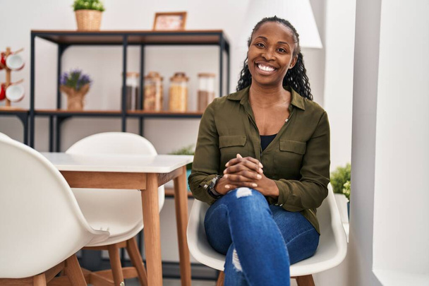Afrikkalainen amerikkalainen nainen hymyilee luottavainen istuu tuolilla kotona - Valokuva, kuva