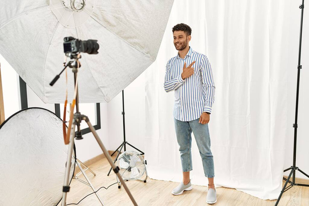 Arab fiatalember pózol, mint modell fotózás stúdió vidám mosollyal az arcon mutató kéz és ujj fel az oldalra boldog és természetes kifejezés  - Fotó, kép