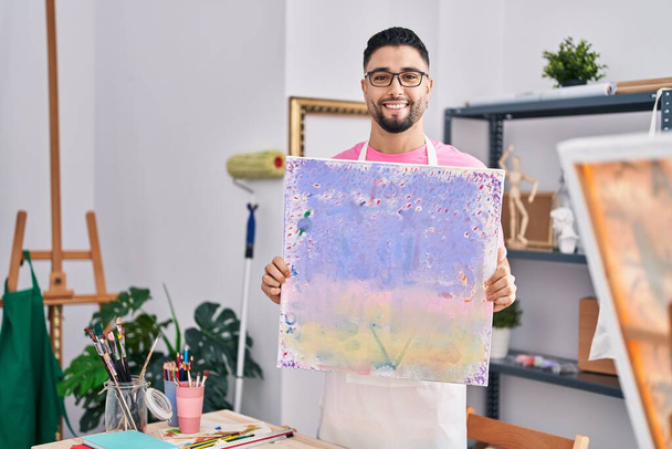 Jonge arabische man kunstenaar glimlachend zelfverzekerd holding draw in kunststudio - Foto, afbeelding