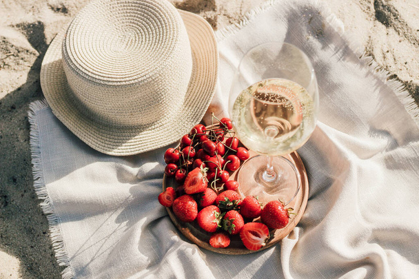Slaměný plážový klobouk s okrajem pro ochranu před sluncem s talířem ovoce a vína. - Fotografie, Obrázek