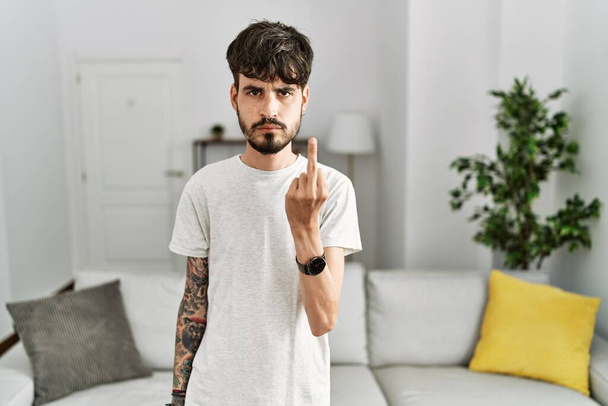 Hispanic man with beard at the living room at home showing middle finger, impolite and rude fuck off expression  - Valokuva, kuva