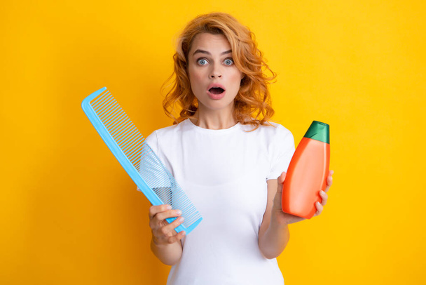 Funny girl combing hair. Redhead woman with a comb, isolated on yellow background. Woman hold bottle shampoo and conditioner. Happy young woman with balm bottle applying hair mask. Beauty product - Fotoğraf, Görsel