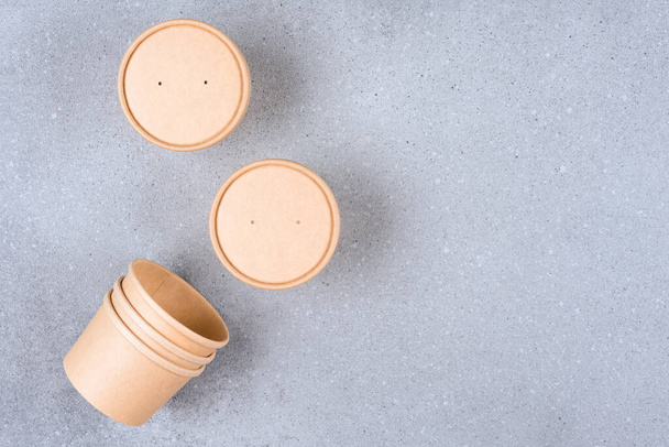 Brown disposable kraft paper soup or ice cream containers, cup with paper cap over gray concrete table background with copy space, mockup image. Sustainable food packaging concept - 写真・画像