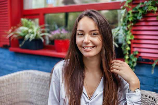 Closeup portrait of young ukrainian beautiful woman smiling and sitting outdoor on cafe terrace with green plant background. Holiday activity and modern lifestyle concept. - Foto, immagini