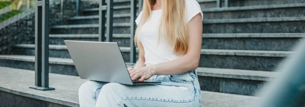 Fiatal diáklány ül laptoppal a lépcsőn, közel az egyetemhez, mosolyog és tanul. web banner. másolás helye - Fotó, kép