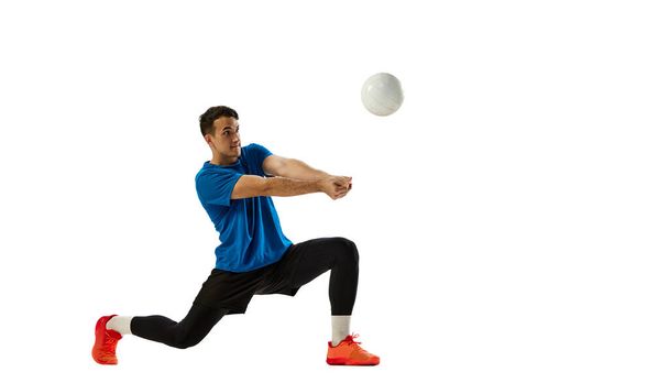 Studio shot of young man, volleyball player in sports uniform playing volleyball isolated on white studio background. Sport, gym, team sport, challenges. Copy space for ad - Фото, зображення