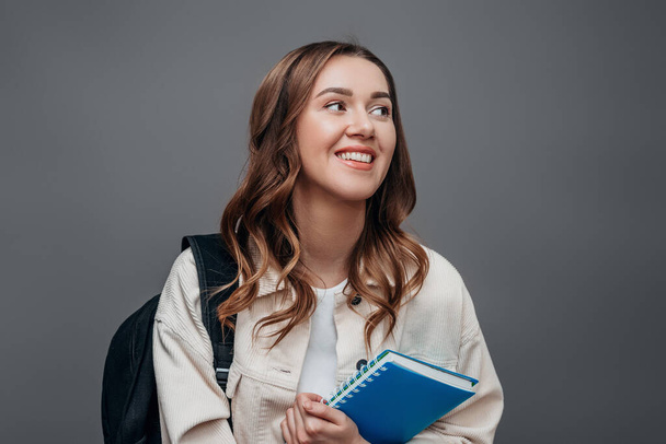 Chica feliz estudiante ríe y sonríe y mirando hacia otro lado sosteniendo un cuaderno aislado sobre fondo gris, espacio para copiar. Chica freelancer feliz - Foto, Imagen