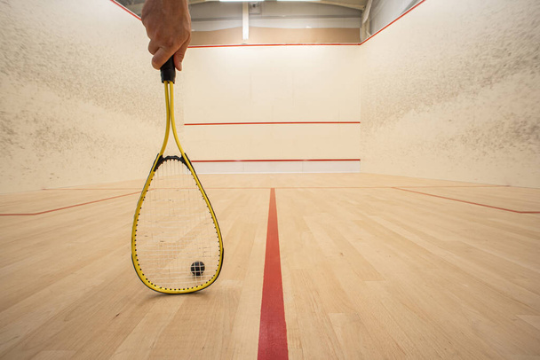 Mão masculina segurando uma raquete dentro de uma quadra de squash. Baixo ângulo, pessoa irreconhecível, grande profundidade de campo - Foto, Imagem