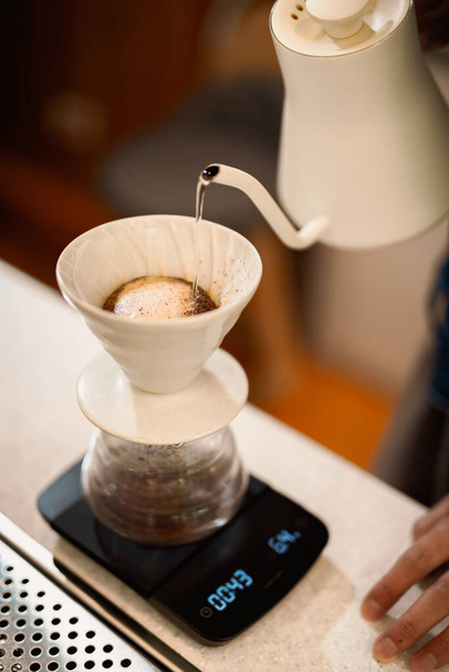 グラウンドコーヒーパウダーの上にケトルから熱湯を注ぐドリップコーヒーを作るバリスタ - 写真・画像