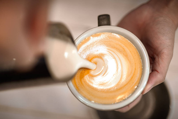 Bovenaanzicht van barista het maken van een kopje veganistische soja koffie latte kunst - Foto, afbeelding