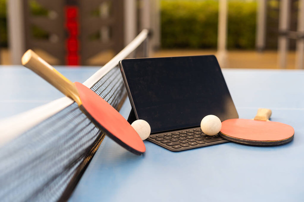 sport, technika, hra a objekty koncept - zblízka ping-pong nebo stolní tenis rakety s míčkem a tablet PC. - Fotografie, Obrázek