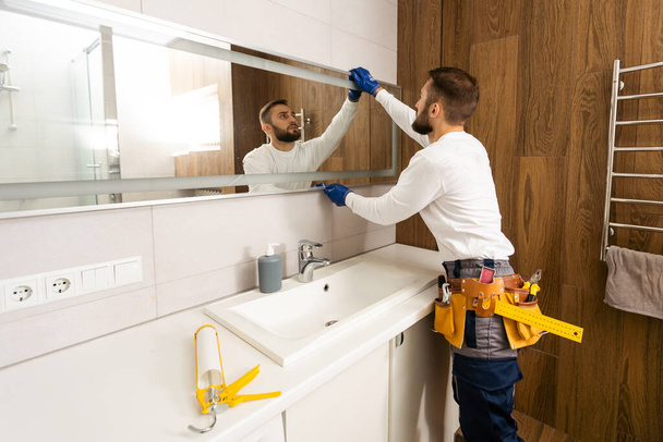 Рабочий устанавливает зеркало в ванной комнате - Фото, изображение