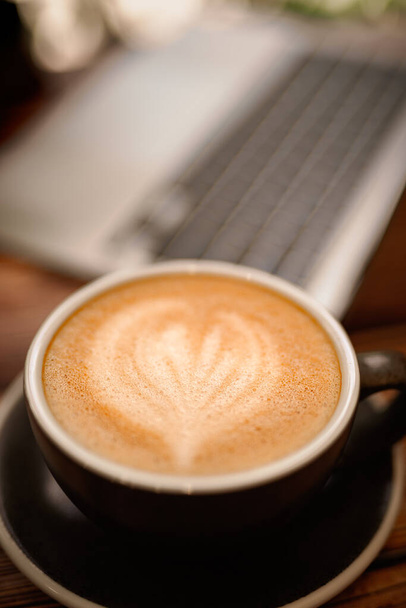 Górny widok na filiżankę gorącej kawy sojowej sztuki z laptopem na drewnianym stole. wygodna koncepcja biurka roboczego. - Zdjęcie, obraz
