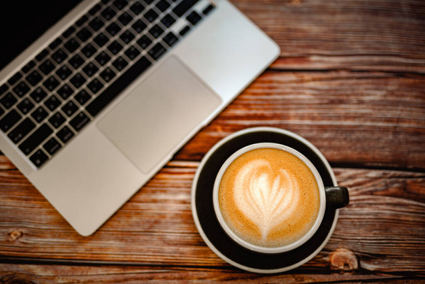 Vue du dessus d'une tasse de café d'art au lait de soja chaud avec ordinateur portable sur une table en bois. concept de bureau de travail confortable. - Photo, image
