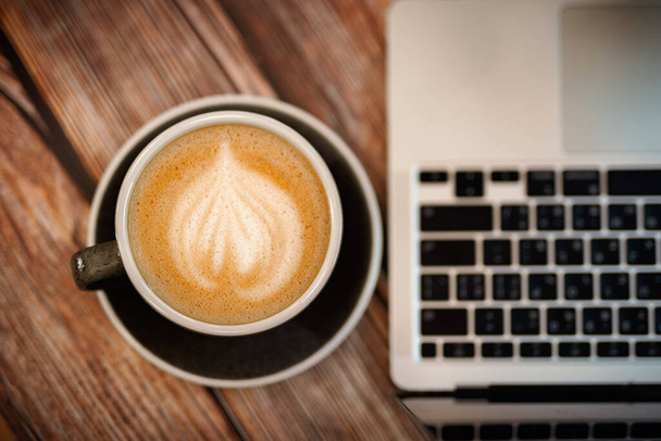 Draufsicht auf eine Tasse heißen Soja-Latte-Art-Kaffee mit Laptop auf einem Holztisch. Komfortables Arbeitsplatzkonzept. - Foto, Bild