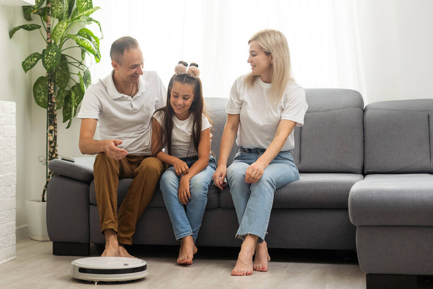 Family resting while robotic vacuum cleaner doing its work at home. - Fotografie, Obrázek