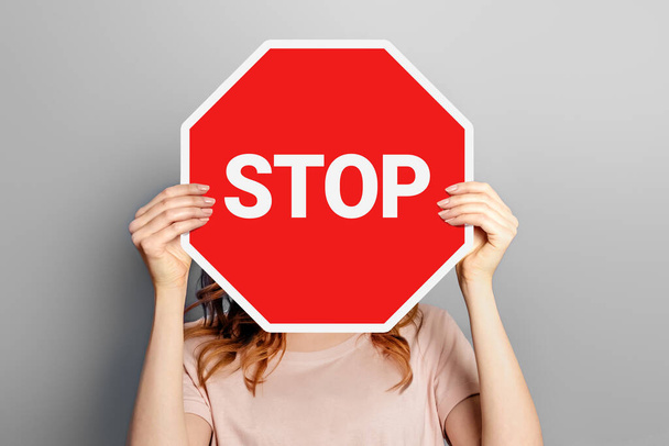 Woman holding poster with stop sign in hands covering her face isolated on grey background - Fotó, kép