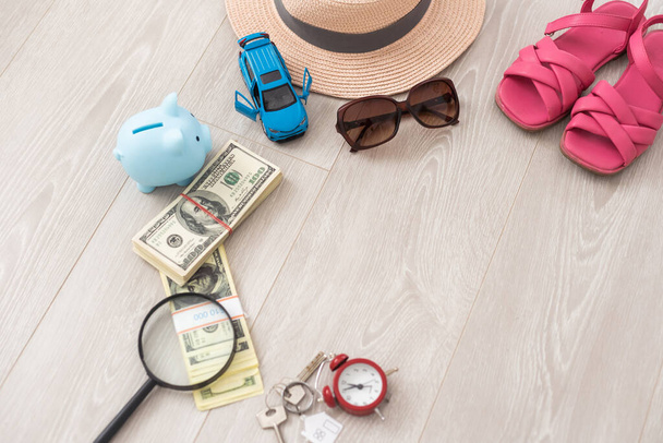 A piggy bank with dollar bills in a travel setting. In the composition of the image: Sun Hat, Alarm Clock. Concept of saving money for traveling on vacation - Foto, Imagen