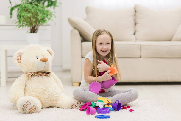 Φωτογραφία του ξανθού κοριτσιού που κοιτάζει στην κάμερα κρατώντας πολύχρωμα παιχνίδια. Έννοια της παιδικής ηλικίας. - Φωτογραφία, εικόνα