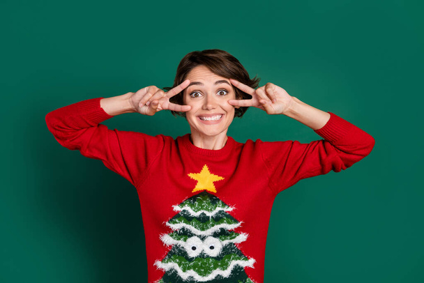 Photo of impressed brown hair young lady show v-sign wear red ugly sweater isolated on green color background. - Fotó, kép