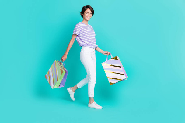 Full length photo of adorable funny girl dressed purple t-shirt smiling walking shopping isolated teal color background. - 写真・画像