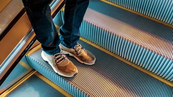 High angle perspective shot detail of man with jeans and sneaker over step mechanical stair - Foto, Bild